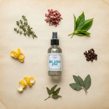 Load image into Gallery viewer, A clear glass spray bottle of Outdoor Bug Shield Spray with a black spray nozzle and a white label in a botanical mandala, set against a parchment background.