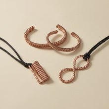 Load image into Gallery viewer, Two twisted copper bracelets alongside an infinity copper pendant and coil pendant necklaces on black cords.