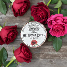 Load image into Gallery viewer, Lip balm container labeled 'Heirloom Roses' with a rose illustration on a wooden surface.