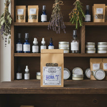 Load image into Gallery viewer, A kraft paper stand-up pouch of Classic Nora T Traditional Herbal Blend by Healing Leaf Apothecary, featuring a white label with blue and black text, set against a rustic apothecary background.