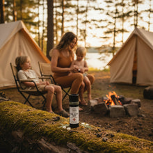 Load image into Gallery viewer, A black cylindrical bottle of Herbal Trail Rescue Balm with a white label, styled on a light beige surface with green leaves, dried flowers, and white tablets.