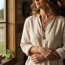 Load image into Gallery viewer, A woman looking out a window wearing copper bracelets and necklaces.
