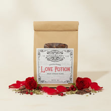 Load image into Gallery viewer, A kraft paper pouch of Cocoa Kissed 'Love Potion' tea on a cream background surrounded with red roses and herbs and berries
