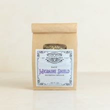 Load image into Gallery viewer, A kraft paper pouch labeled 'Migraine Shield' with a clear window showing dried herbs inside, displayed on a neutral background
